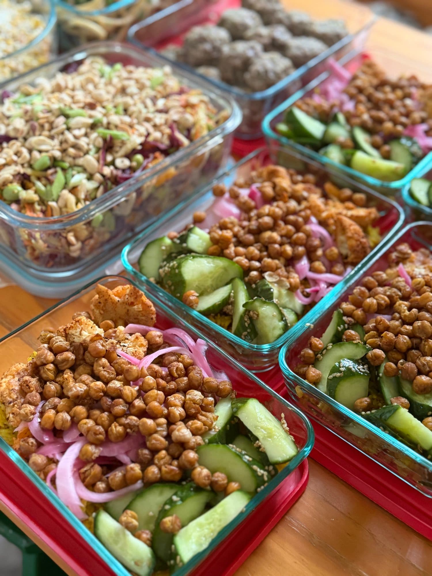 Matching containers of roasted chickpeas, cauliflower, pickled onion, and cucumber, portioned side by side