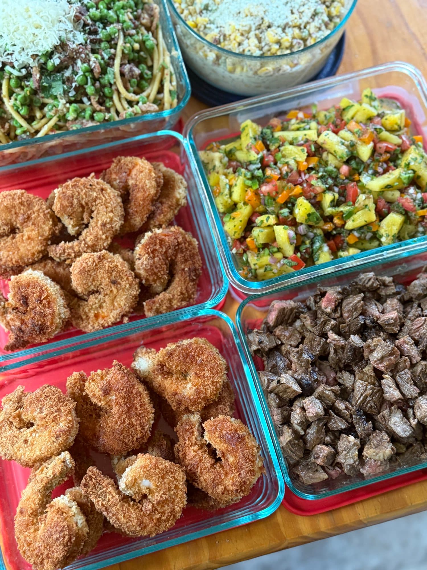 Prepped containers of crusted shrimp, seared steak, mango salsa, spaghetti with peas, and elote corn salad