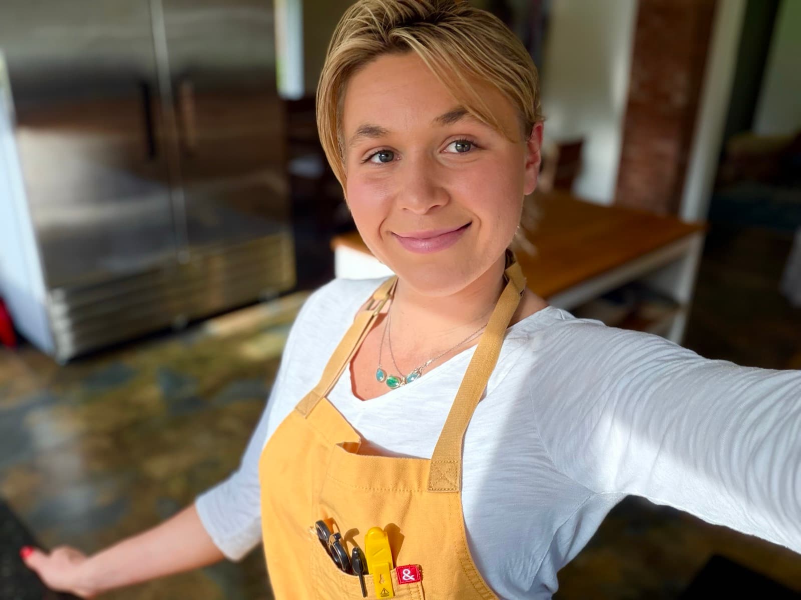 Sarah in a client kitchen, yellow apron on, smiling