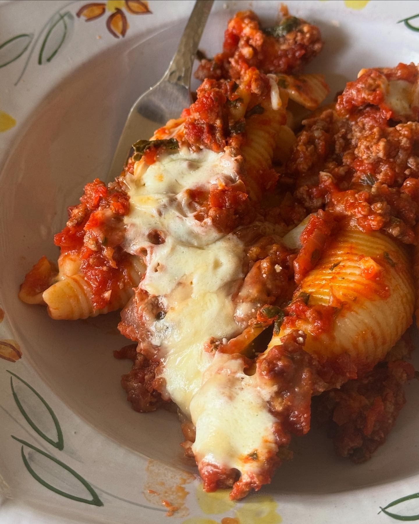 Baked stuffed shells with meat sauce and melted mozzarella on a hand-painted plate